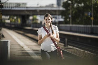 Schöne junge Frau hört Musik über ihr Handy, während sie auf dem Bahnsteig spazieren geht - UUF20894