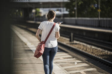 Frau benutzt Mobiltelefon beim Gehen auf dem Bahnsteig - UUF20895