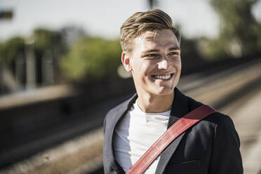 Lächelnder gut aussehender junger Mann, der am Bahnhof steht und wegschaut - UUF20904