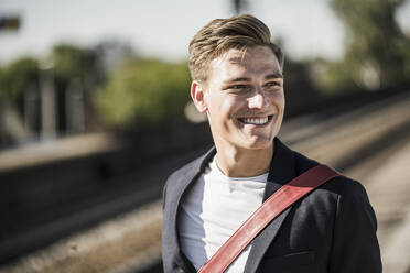 Smiling handsome young man looking away while standing at railroad station - UUF20904