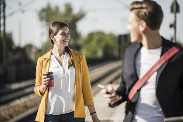 Lächelnde Frau mit wiederverwendbarem Kaffeebecher, die beim Gehen am Bahnsteig wegschaut - UUF20909