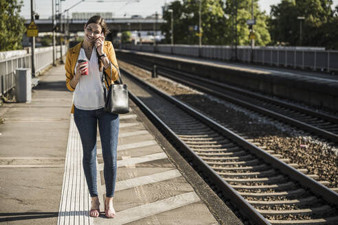 Lächelnde Frau, die auf dem Bahnsteig stehend mit ihrem Handy telefoniert - UUF20911