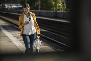 Junge Frau benutzt ihr Smartphone, während sie auf dem Bahnsteig spazieren geht - UUF20912