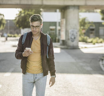 Junger Mann, der sein Smartphone benutzt, während er in der Stadt auf der Straße geht - UUF20917