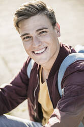 Lächelnder, gut aussehender junger Mann in Freizeitkleidung, der im Freien sitzt - UUF20922