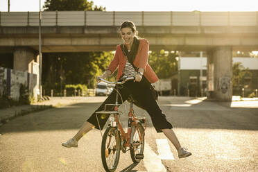 Fröhliche junge Frau genießt das Radfahren auf der Straße an einem sonnigen Tag - UUF20931