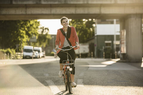 Happy young woman riding bicycle on street in city stock photo