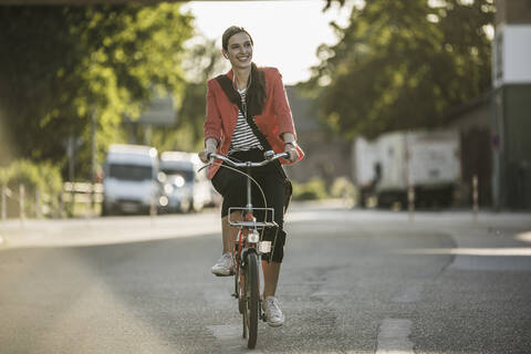 Smiling young woman riding bicycle on street in city stock photo