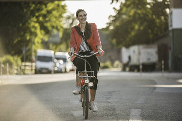 Smiling young woman riding bicycle on street in city - UUF20934