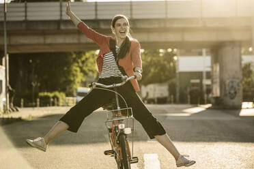Fröhliche Frau genießt das Radfahren auf der Straße in der Stadt an einem sonnigen Tag - UUF20935