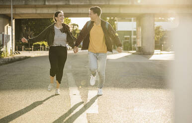Carefree young couple holding hands while running on street in city - UUF20938