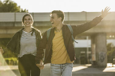 Cheerful couple holding hands while running on street in city - UUF20939