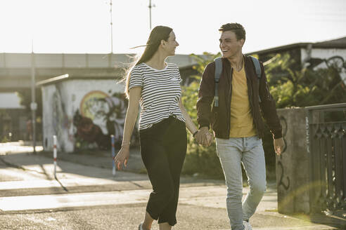 Happy young couple holding hands while walking on street - UUF20940