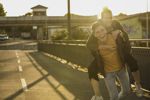 Verspielter Freund nimmt seine Freundin an einem sonnigen Tag in der Stadt huckepack - UUF20955