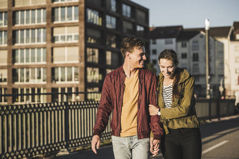 Smiling young couple holding hands while walking in city - UUF20956