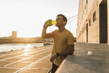 Man drinking water after workout against clear sky - UUF20963
