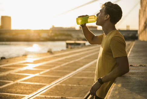 Man drinking water after workout against clear sky - UUF20971