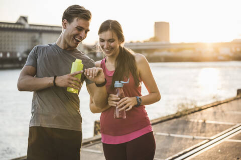Lächelnde Freunde mit Wasserflasche, die die Zeit im Hafen überprüfen, lizenzfreies Stockfoto