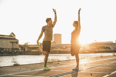 Friends exercising with arms raised at harbor during sunny day - UUF20981