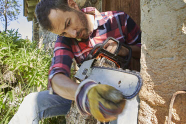 Lumberjack sharpening chainsaw while sitting against structure - VEGF02763
