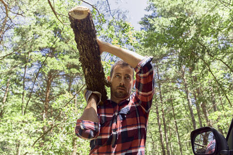 Lumberjack carrying log on shoulder in forest stock photo