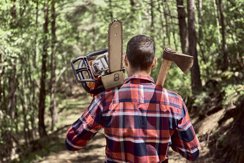 Lumberjack with chainsaw and axe walking in forest stock photo