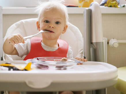Süßes kleines Baby beißt Gabel, während auf Hochstuhl in der Küche sitzen - KNTF05189