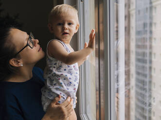 Frau mit kleinem Sohn am Fenster zu Hause - KNTF05195
