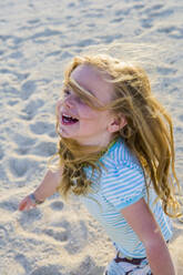 Laughing 3 year old girl running in the sand - MINF15107