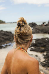 Rückansicht einer Frau am Strand mit Blick auf einen Felsen - MINF15114