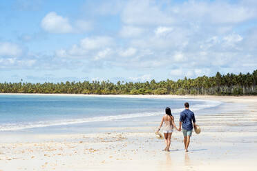 Ein gut aussehendes hispanisches (lateinamerikanisches) Paar, das mit dem Rücken zur Kamera an einem einsamen Strand spazieren geht, Brasilien, Südamerika - RHPLF17379