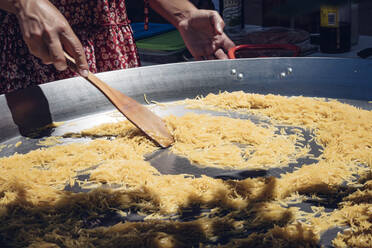 Woman preparing a spanish fideuá with squid prawns and noodles in a paella pan - CAVF88364