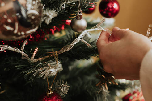 Anonyme Person, die zu Weihnachten eine Lichtergirlande an einen Nadelbaum hängt - CAVF88386