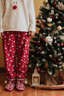 Frau im warmen Pyjama in der Nähe einer geschmückten Fichte am ersten Weihnachtsfeiertag - CAVF88387