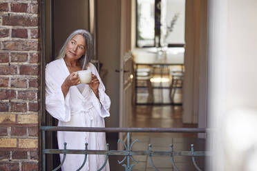 Lächelnde Frau, die auf dem Balkon stehend Tee trinkt - MCF01104
