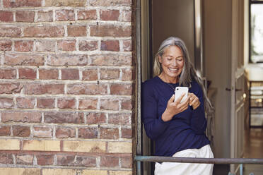 Smiling woman using phone in balcony - MCF01114