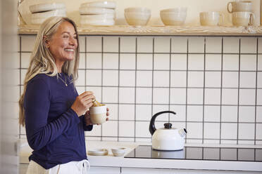Lächelnde Frau trinkt Tee, während sie in der Küche steht - MCF01122