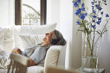 Smiling woman with closed eyes enjoying music in living room - MCF01130