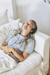 Thoughtful woman listening to music in living room - MCF01135