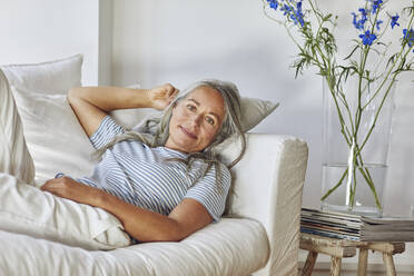 Lächelnde Frau entspannt sich und liegt auf dem Sofa im Wohnzimmer - MCF01146