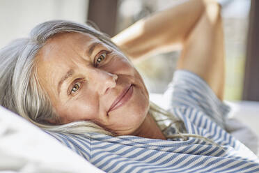 Close-up of smiling woman relaxing with hands behind hand in living room - MCF01163