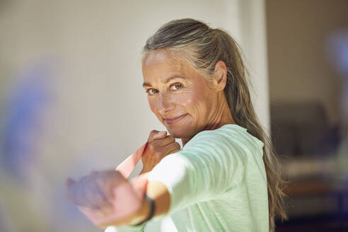 Smiling woman exercising with resistance band at home - MCF01173