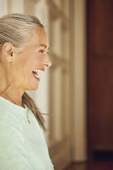 Cheerful wrinkled woman looking away against door at home - MCF01176