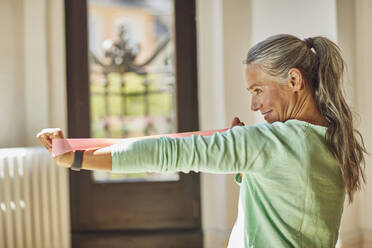 Smiling woman exercising with resistance band in living room - MCF01183