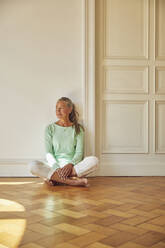 Thoughtful woman sitting on floor by door at home - MCF01186