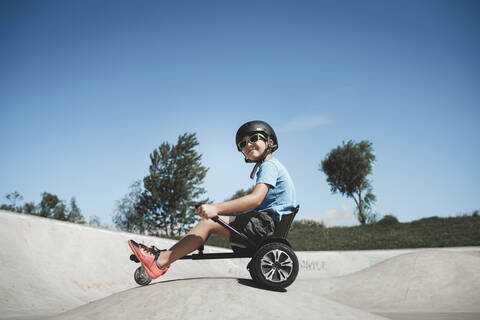 Little boy sitting on hoverkart at skateboard park during sunny day stock photo