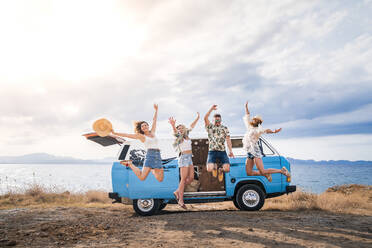 Fröhlicher Tourist springt mit erhobenen Händen und Beinen auf dem Hintergrund eines hellen Minivans am Strand in einem sonnigen Tag - ADSF11219