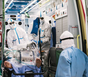 Eine Gruppe von Ärzten in Schutzkleidung steht in einem Krankenwagen mit Ausrüstung und bereitet sich auf den Transport von Patienten vor - ADSF11240