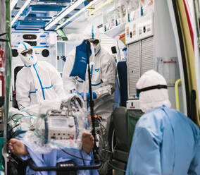 Group of professional doctors in protective uniform standing in ambulance car with equipment and preparing for patient transportation - ADSF11240