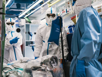 Group of professional doctors in protective uniform standing in ambulance car with equipment and preparing for patient transportation - ADSF11242